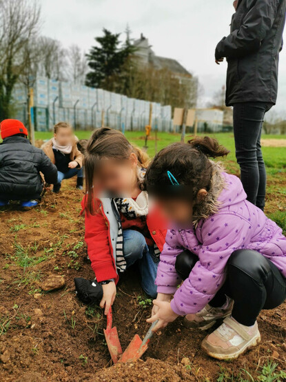 Deux enfants creusent la terre avec des pelles pour planter un arbre.